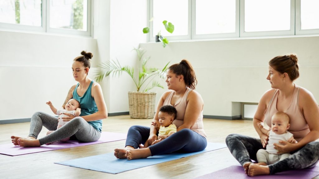 three moms sit on yoga mats at a baby & me yoga class